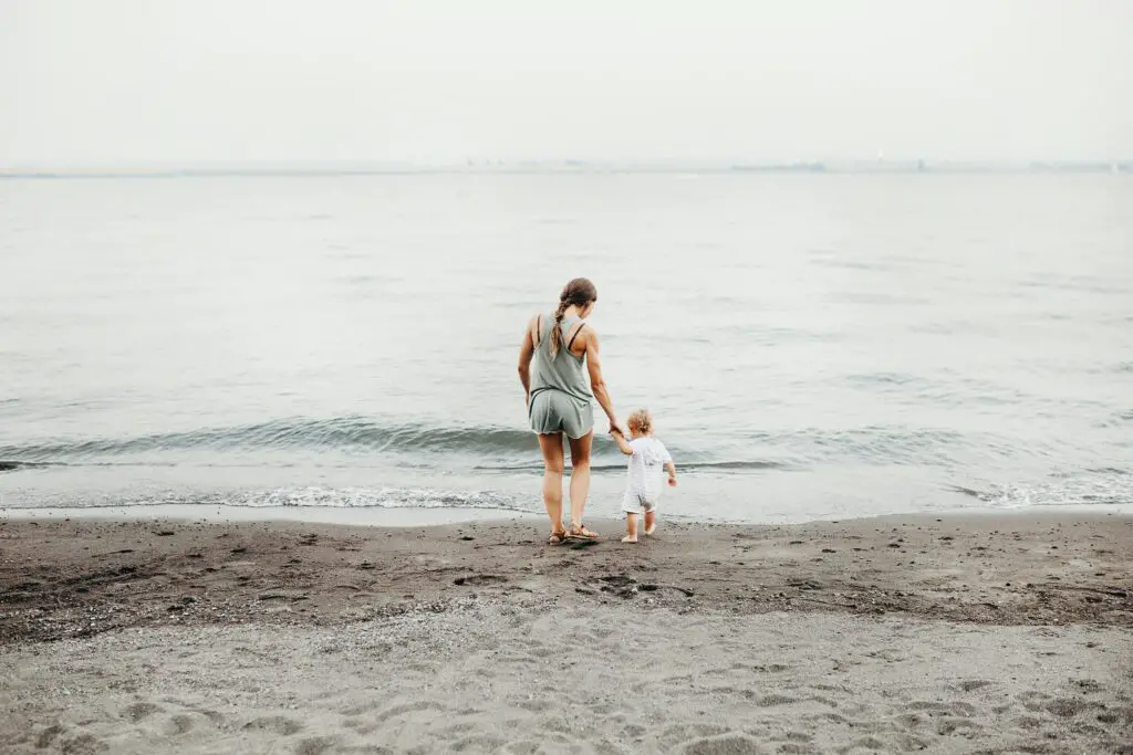 Midlife mom walking with toddler on the beach