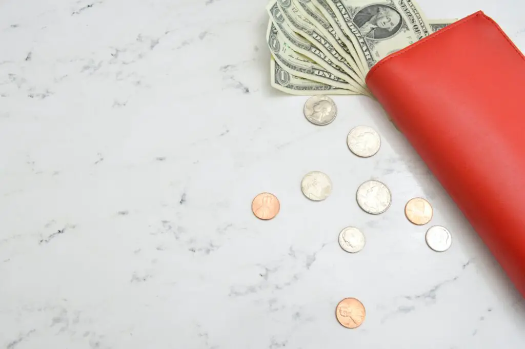 Low buy year- red wallet with dollar bills and loose coins on a marble surface