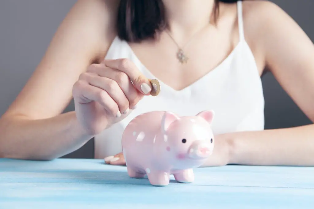 Woman putting money into a small, pink piggy bank