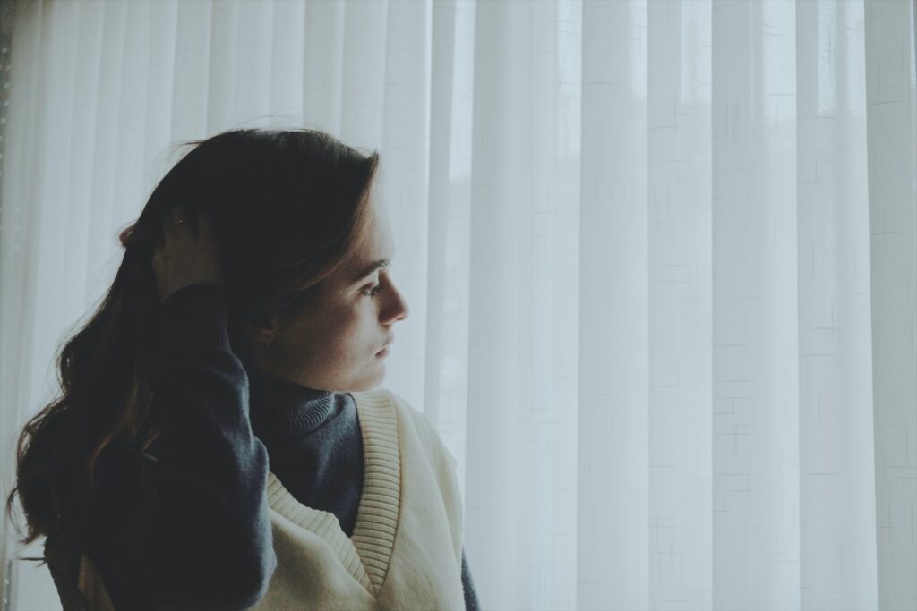 Photo of worried woman standing next to a window. Premenstrual. dysphoric disorder PMDD can cause feelings of anxiety and hopelessness.